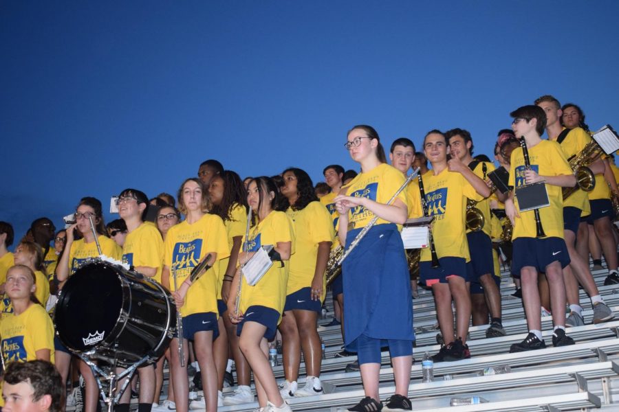 The band watches the football game as they prepare to play.